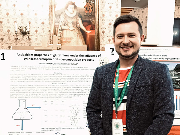 A smiling man in a dark blazer stands in front of a poster presenting the results of his research