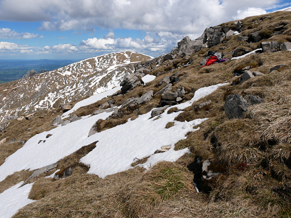 A gentle, stony-grassy mountainside. Here and there are remnants of melting snow